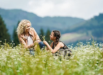 Mutter und Tochter sitzen auf der Wiese beim Hotel Unterschwarzachhof in Saalbach Hinterglemm