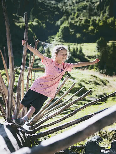 Girl balancing on a tree trunk at the head of the valley in Saalbach Hinterglemm